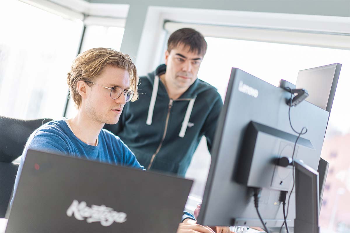 A man is working on a computer, and another is observing him